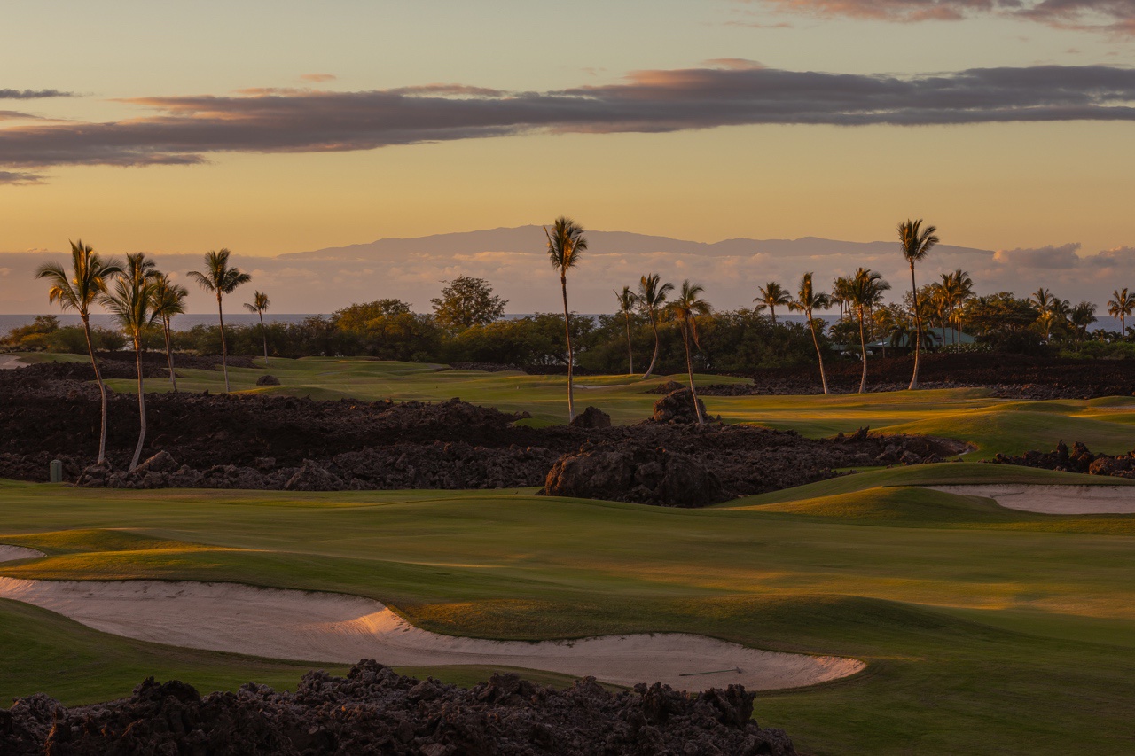 Waimea Vacation Rentals, 5BD Mauna Lani Lux Golf Estate (4) at One Ocean - As the sun sets, the soft golden light enhances the serene beauty of this golf course, highlighting the lush green fairways edged by contrasting black volcanic rock and scattered palm trees.