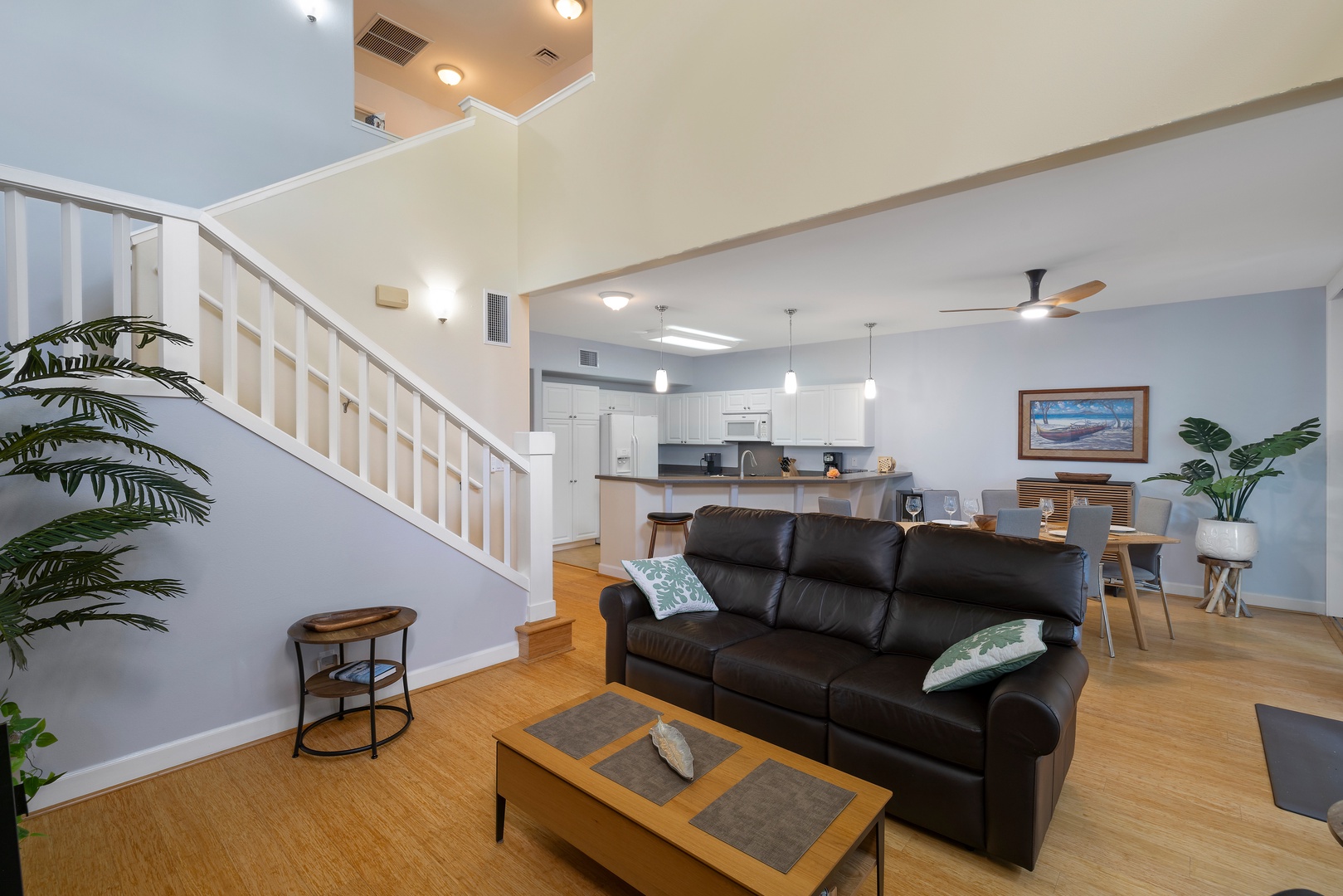 Unwind in your spacious open-concept living area with plush leather seating, warm hardwood floors, and tropical plants creating a welcoming atmosphere.