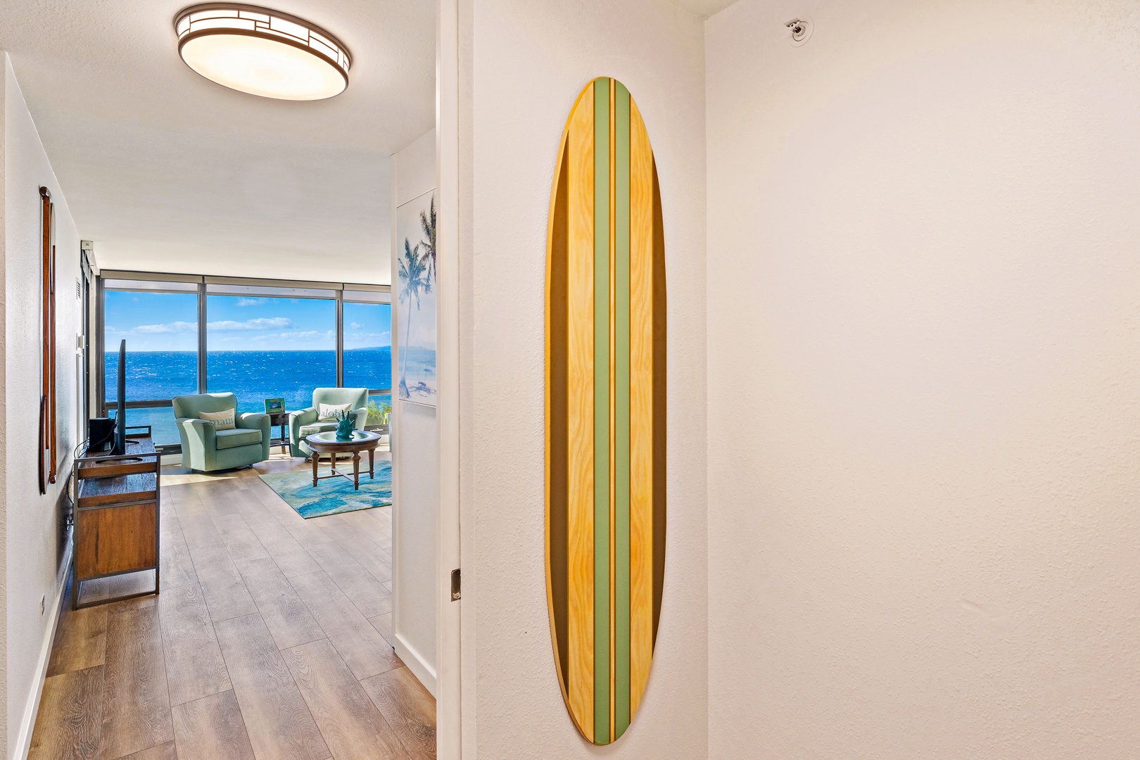 Lahaina Vacation Rentals, Mahana 718 - A decorative surfboard adds a touch of coastal charm to the hallway, leading into the bright and inviting living area.