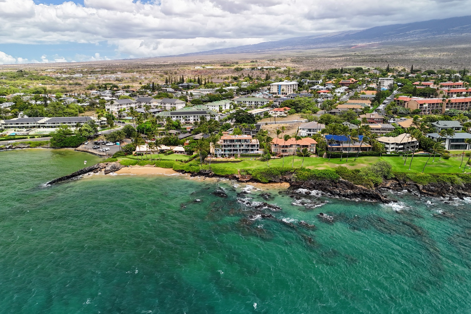 Kihei Vacation Rentals, Punahoa Beach 205 - The coastline curves past lava rock and green, with the beach cove at its center.