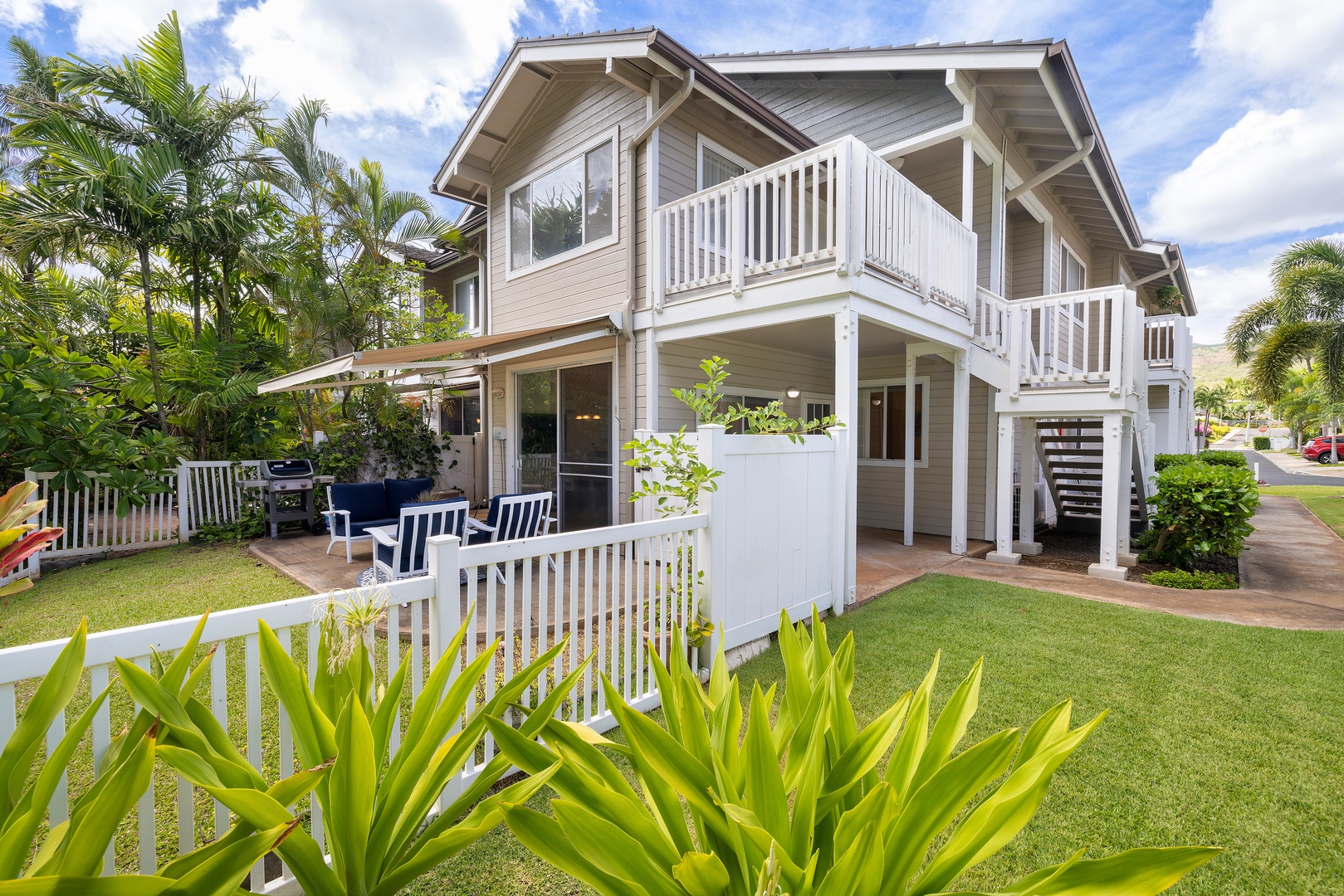 Modern two-story property featuring tropical landscaping and covered outdoor dining areas surrounded by lush palm trees and manicured gardens.