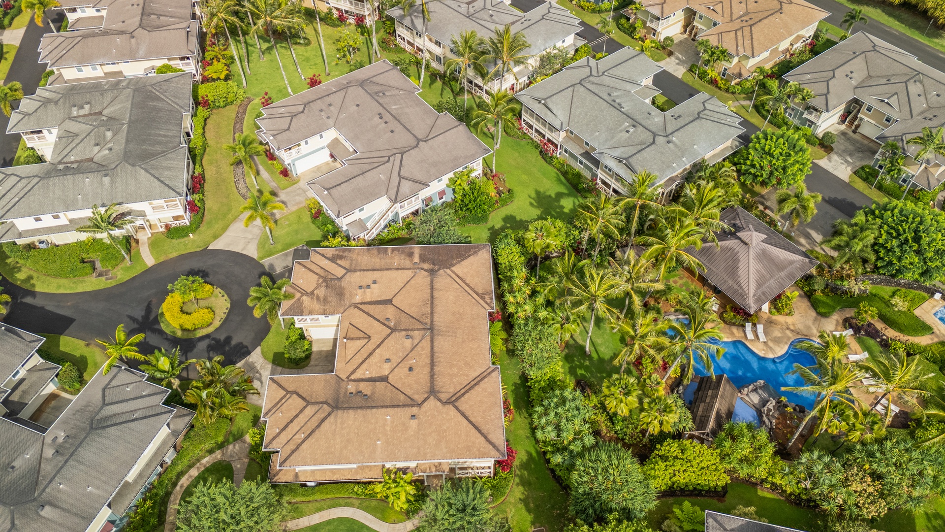 Princeville Vacation Rentals, Kaimana Villa - Aerial view of tropical residential neighborhood with palm trees, lush landscaping, and nearby swimming pool amenities in a peaceful suburban setting.