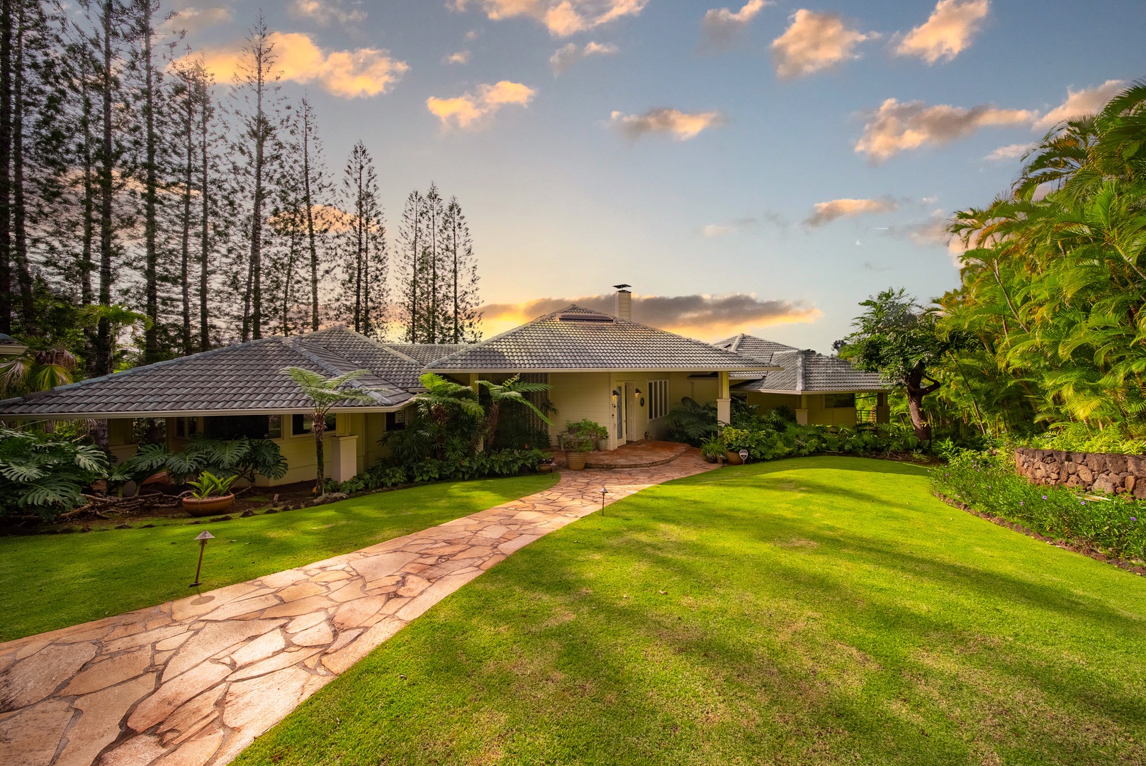 Haleiwa Vacation Rentals, Ka Hale Hau'oli - Stunning tropical property surrounded by lush gardens and towering palms, captured during golden hour with dramatic clouds overhead.
