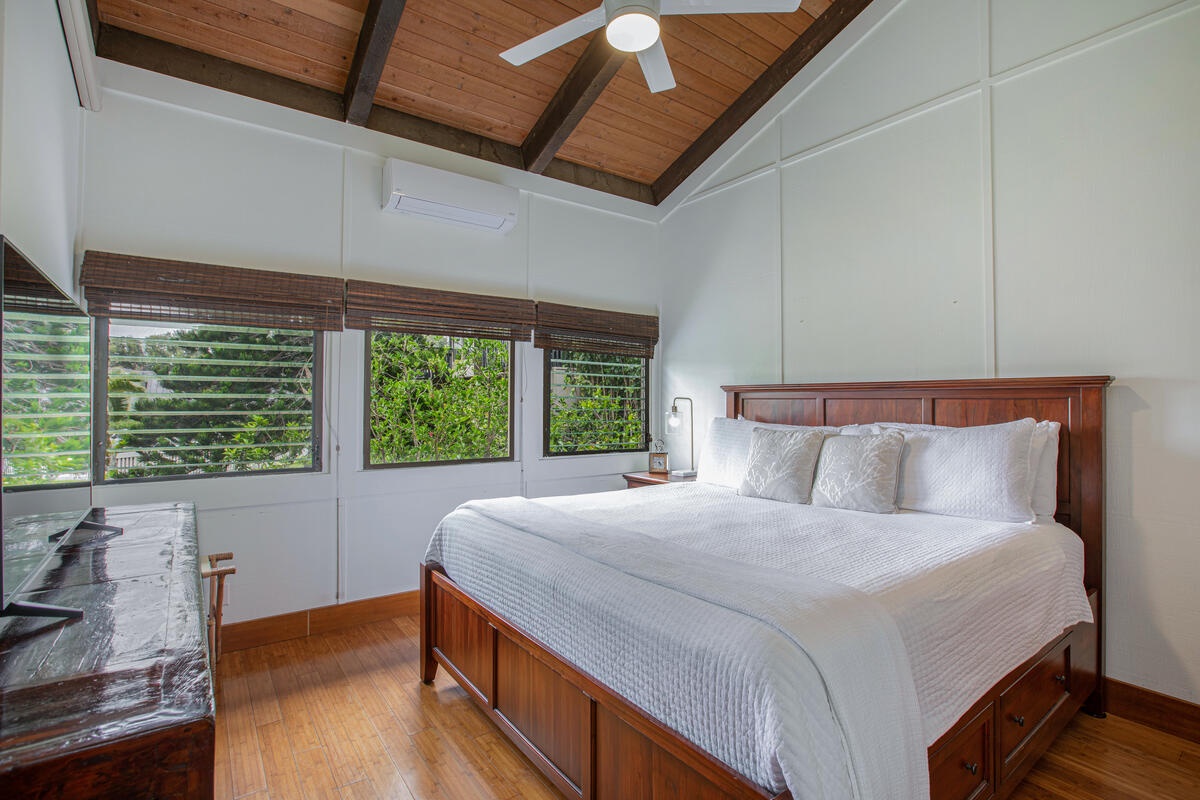 Princeville Vacation Rentals, Mauna Kai 11 - Primary suite with king bed, A/C, and picture windows framing tropical greenery.