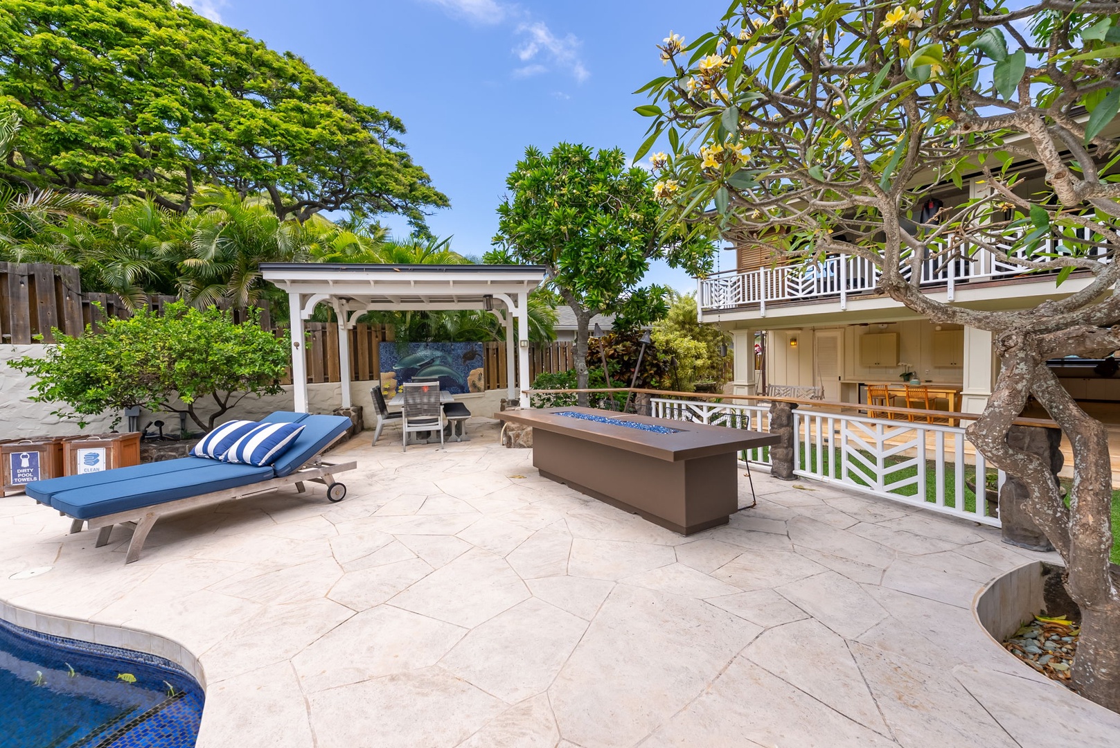 Kailua Vacation Rentals, Leaf House - A private outdoor retreat featuring a spacious patio with loungers and fire pit table, surrounded by tropical trees and a pergola-covered seating nook.