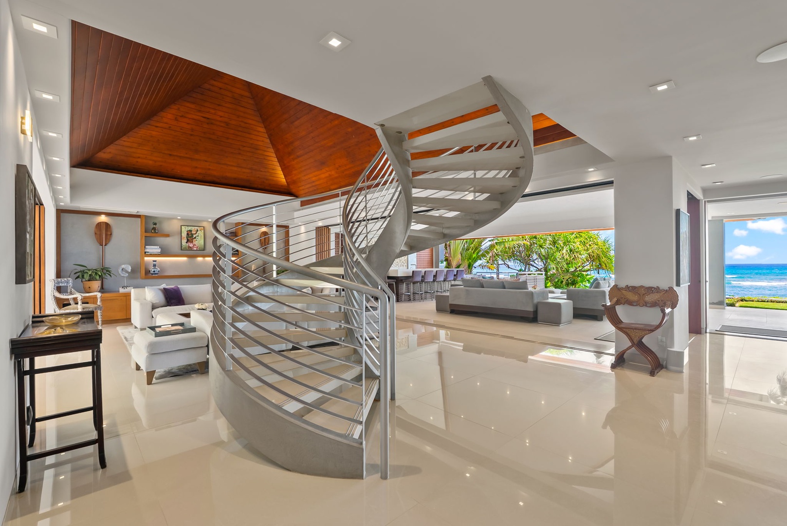 Honolulu Vacation Rentals, Diamond Head Beachfront Estate - A dramatic spiral staircase anchors this bright, open-plan living space featuring polished tile floors, striking wood ceilings, and stunning ocean views beyond.