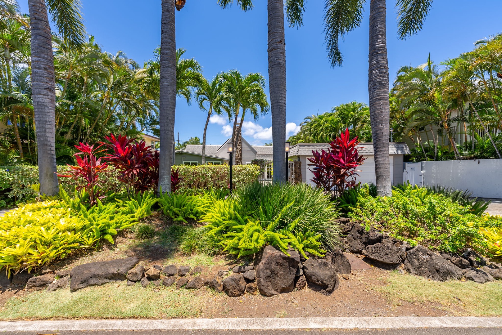 Honolulu Vacation Rentals, Ho'okipa Villa - Tropical landscaping surrounds the property with palm trees, volcanic rock accents, and vibrant red and green foliage creating a lush Hawaiian ambiance.
