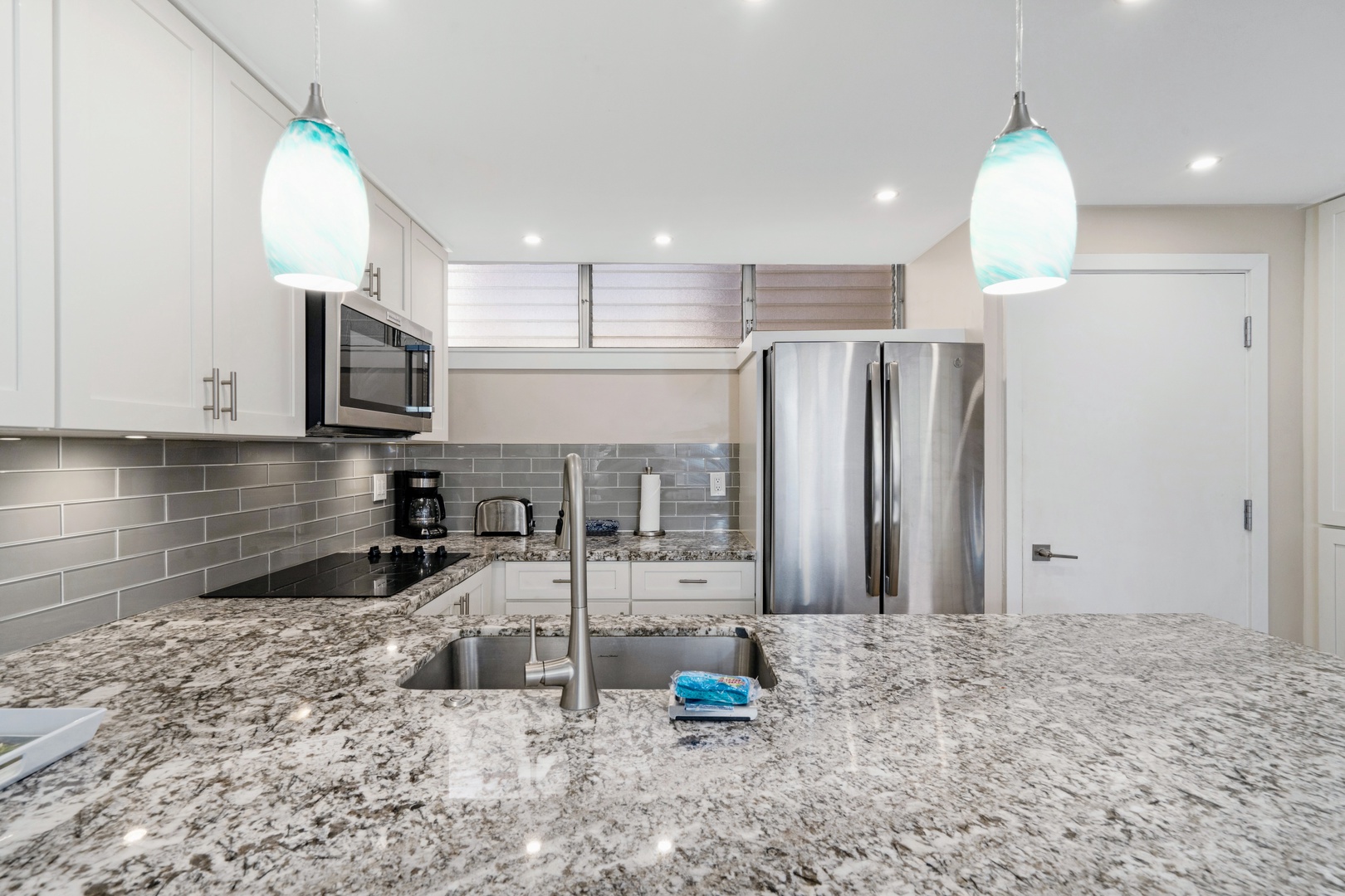 Kihei Vacation Rentals, Haleakala Shores A206 - A glass cooktop and a coffee station line up under the gray subway tile, ready before anyone's fully awake.