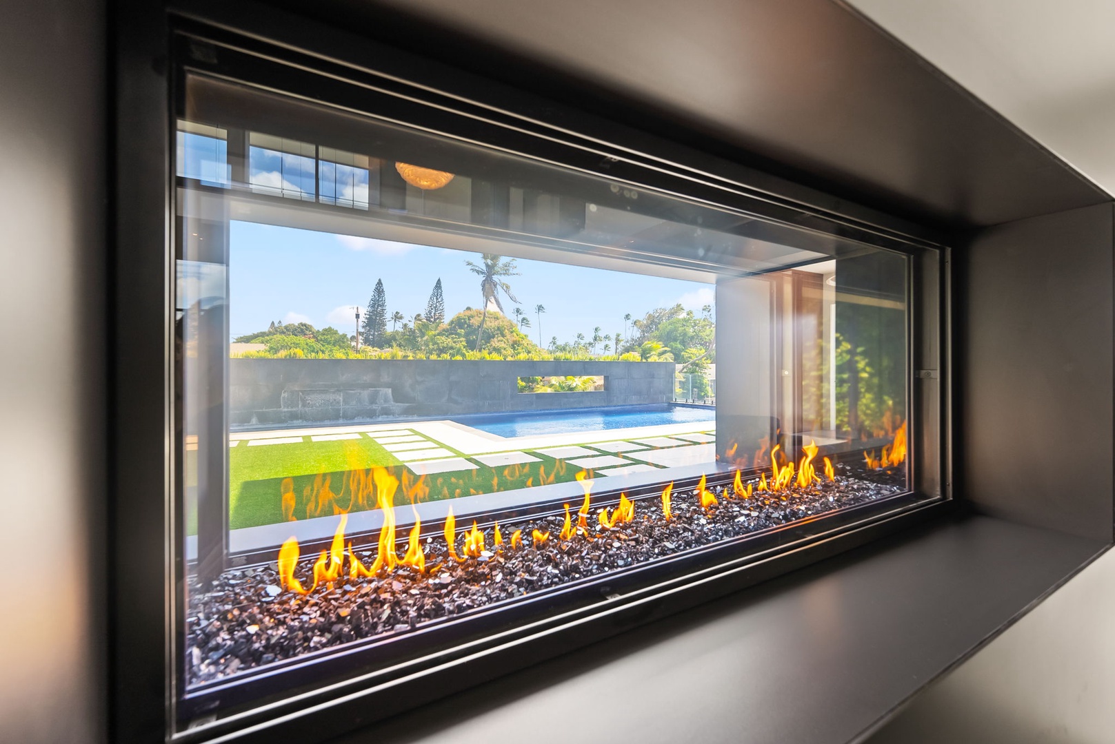 Honolulu Vacation Rentals, Ocean Villa 3 Bedroom - Modern see-through fireplace framing glowing flames and serene pool views beyond.