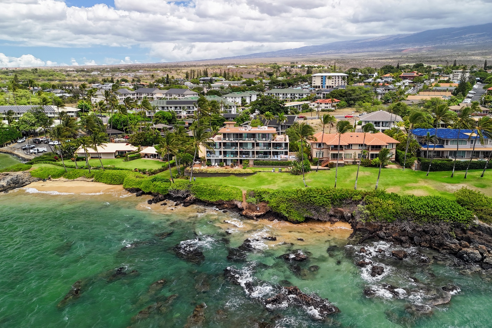 Kihei Vacation Rentals, Punahoa Beach 205 - Green ridges rise behind the rooftops, with a crescent of beach cut into the shoreline below.