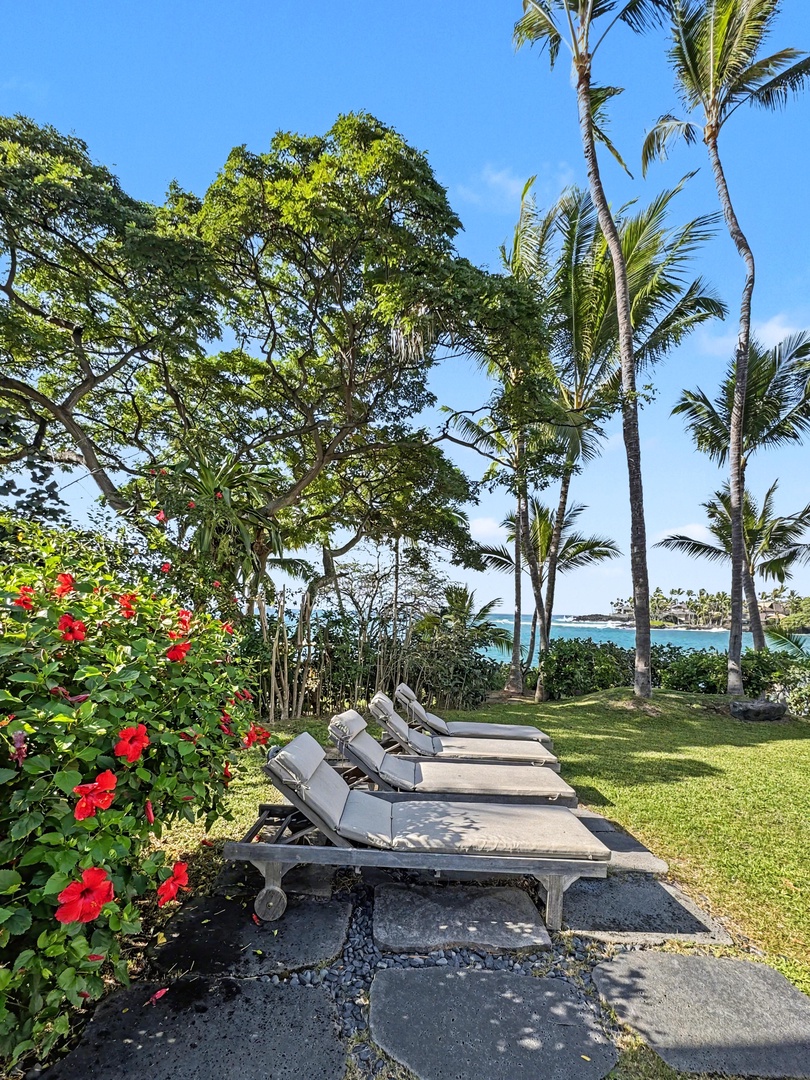 Kailua-Kona Vacation Rentals, Hahalua Bay Villa - Tropical paradise lounge area with oceanfront chaise loungers surrounded by vibrant hibiscus blooms and swaying palms overlooking turquoise waters.