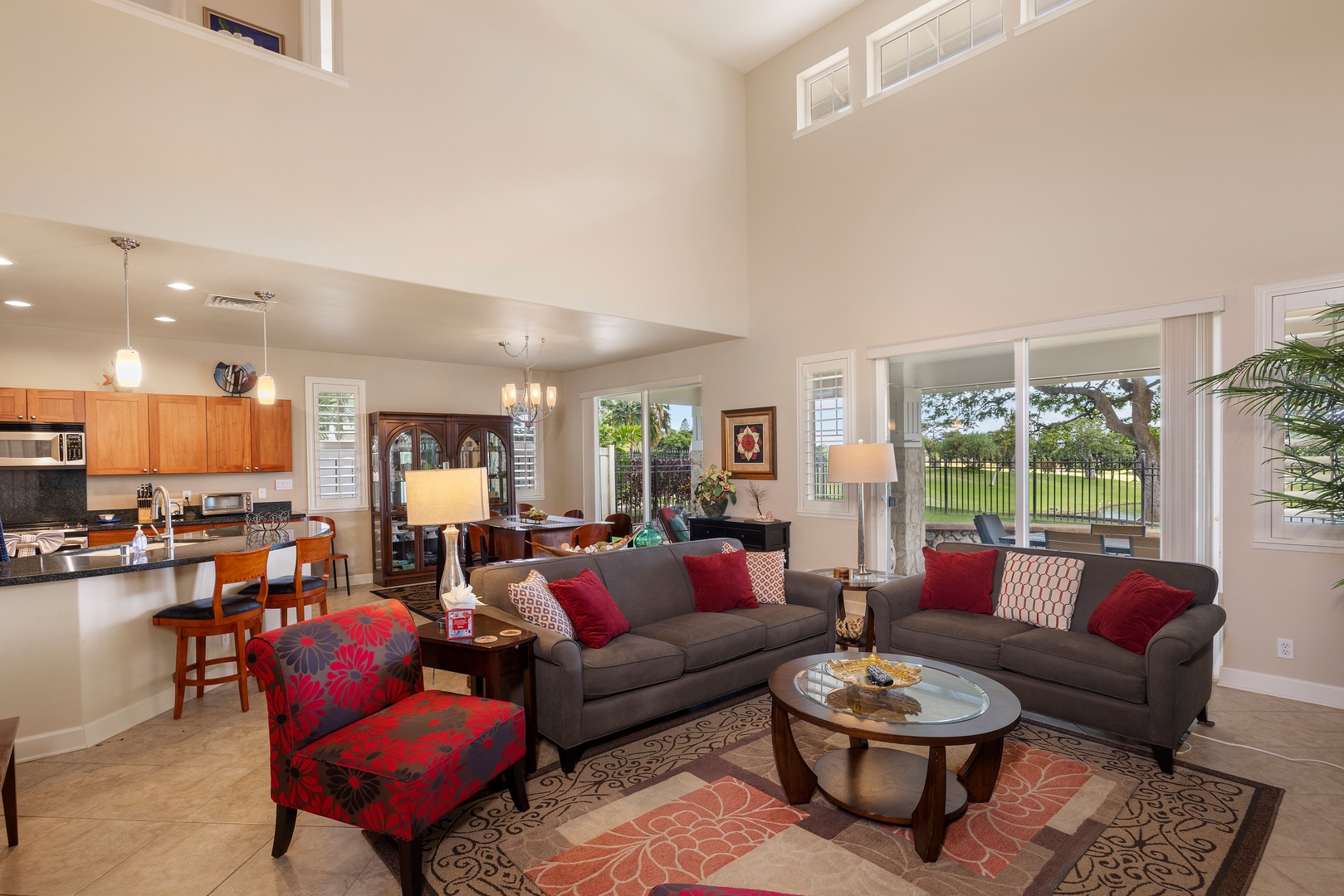 Relax in your spacious open-plan living area with soaring ceilings, where plush gray sofas and vibrant red accents create the perfect setting for memorable evenings together.