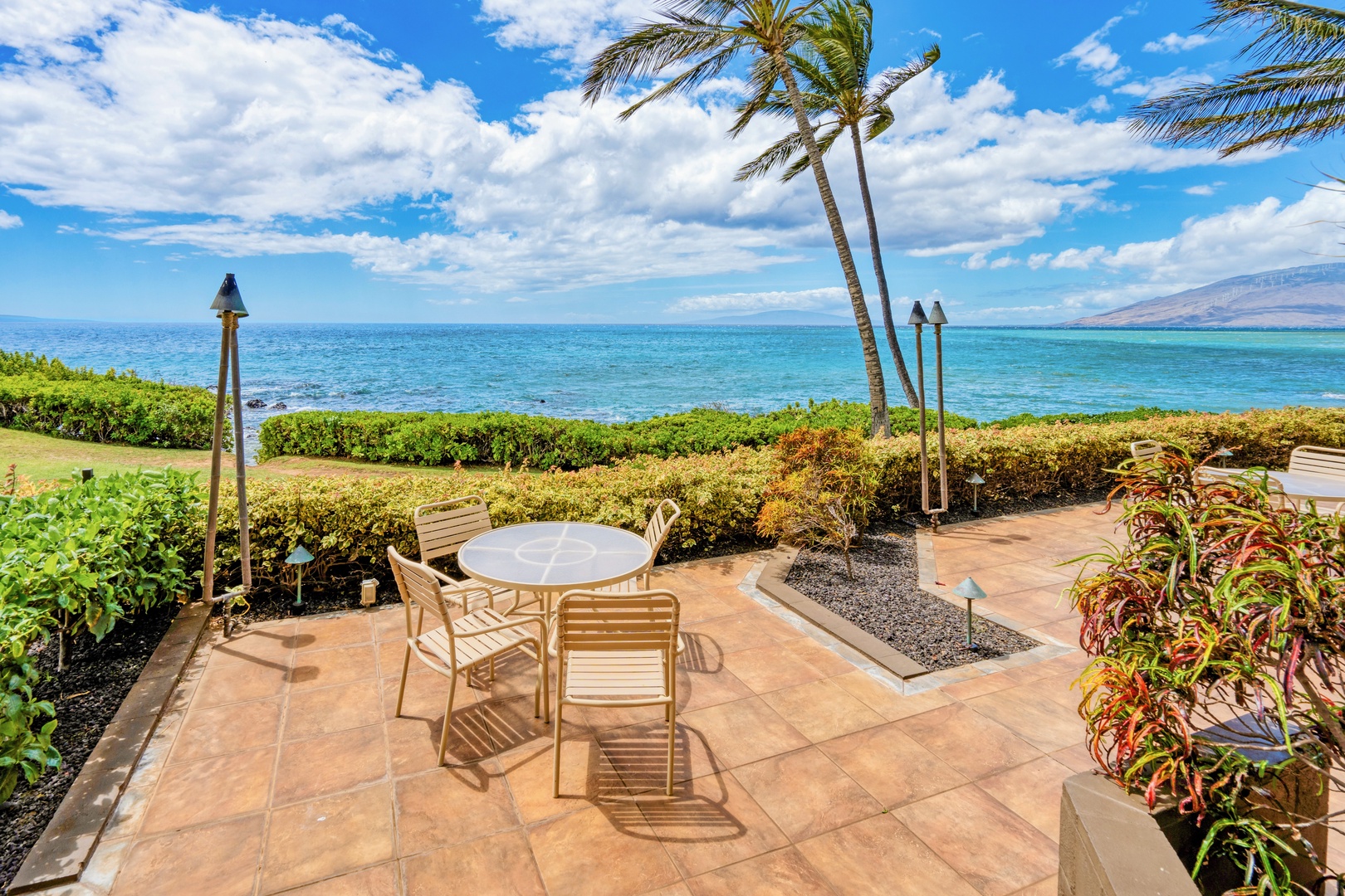 Kihei Vacation Rentals, Punahoa Beach 205 - Tiki torches flank the patio table, palms swaying against a wide stretch of blue.