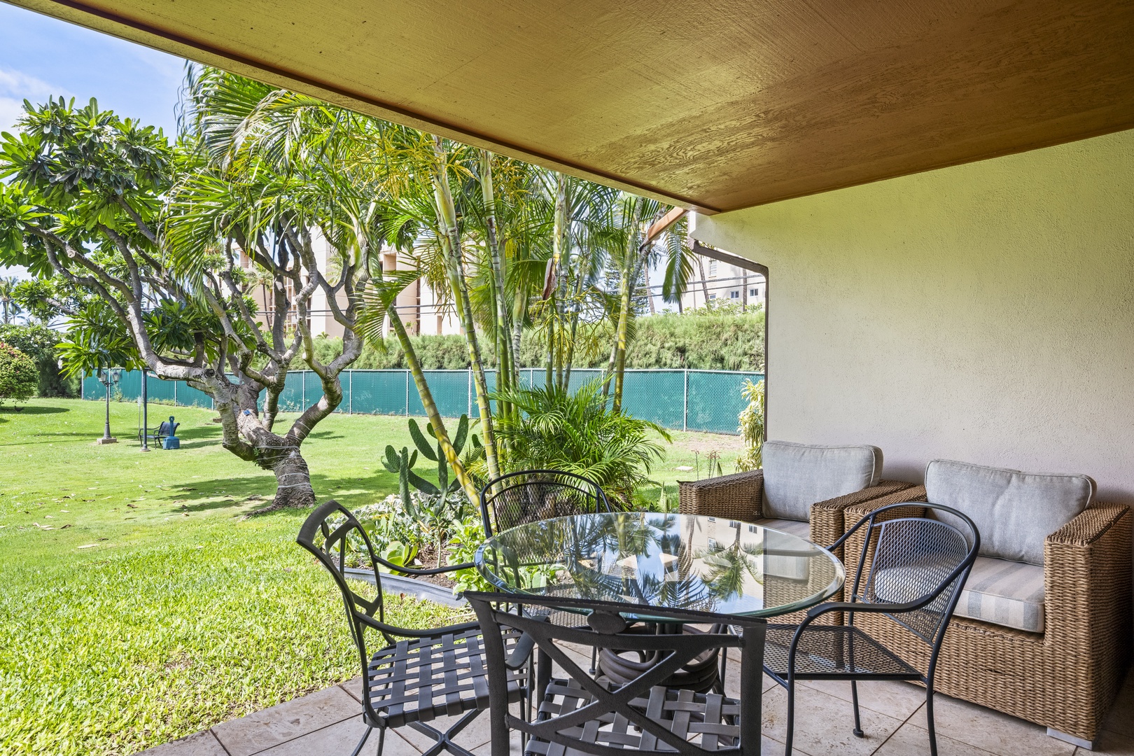 Kihei Vacation Rentals, Koa Resort 1B - Afternoon reading on the shaded lanai, the lawn stretching green just past the chairs.