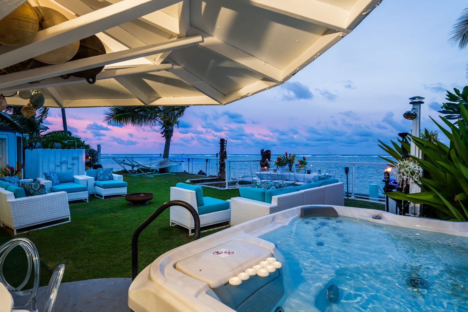 Hauula Vacation Rentals, Private Beach Paradise - Oceanfront lanai at twilight with a hot tub, lounge seating, and peaceful coastal views.
