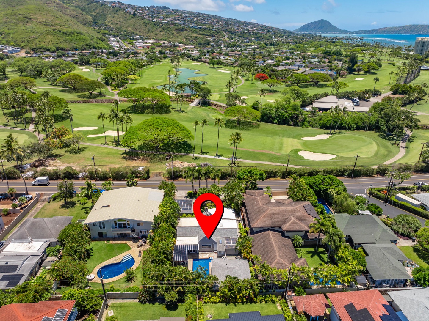 Honolulu Vacation Rentals, Ho'okipa Villa - Aerial view of the property nestled in a coastal neighborhood with a championship golf course directly across the street, surrounded by lush tropical landscaping and framed by dramatic mountain and ocean vistas.
