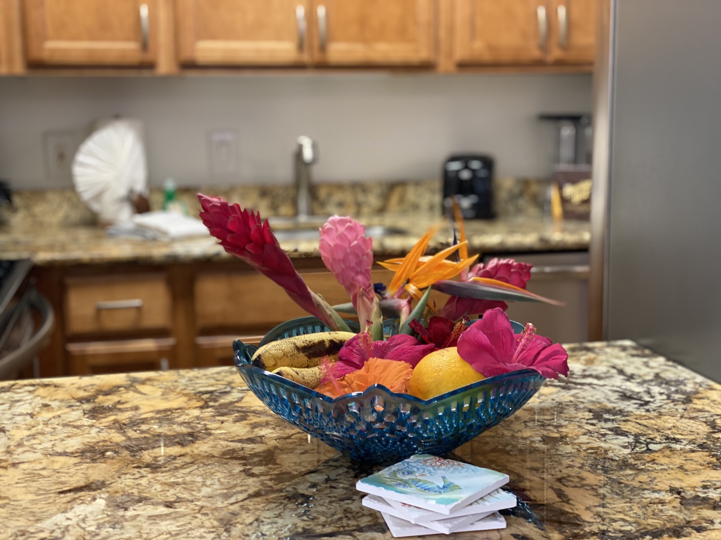 Lahaina Vacation Rentals, Royal Kahana 213 - A decorative bowl with vibrant tropical flowers adds a welcoming island touch to the kitchen counter, creating a warm and inviting atmosphere.