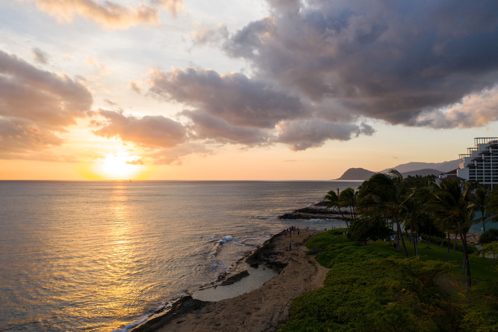 Kapolei Vacation Rentals, Ko Olina Beach Villas B604 - Stunning beachfront location with golden sunset views over the ocean, palm trees, and nearby resort buildings creating a tropical paradise setting.
