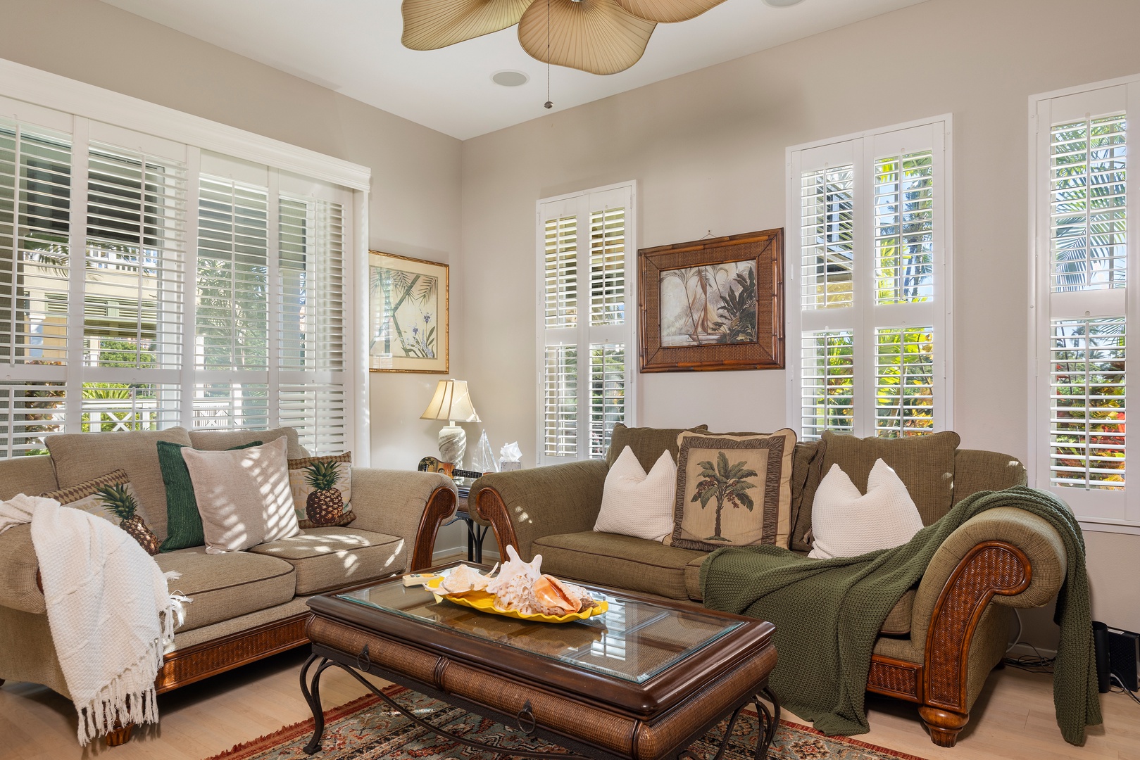 Relax in your tropical-inspired living room where warm sunlight filters through plantation shutters, creating the perfect spot for afternoon leisure.