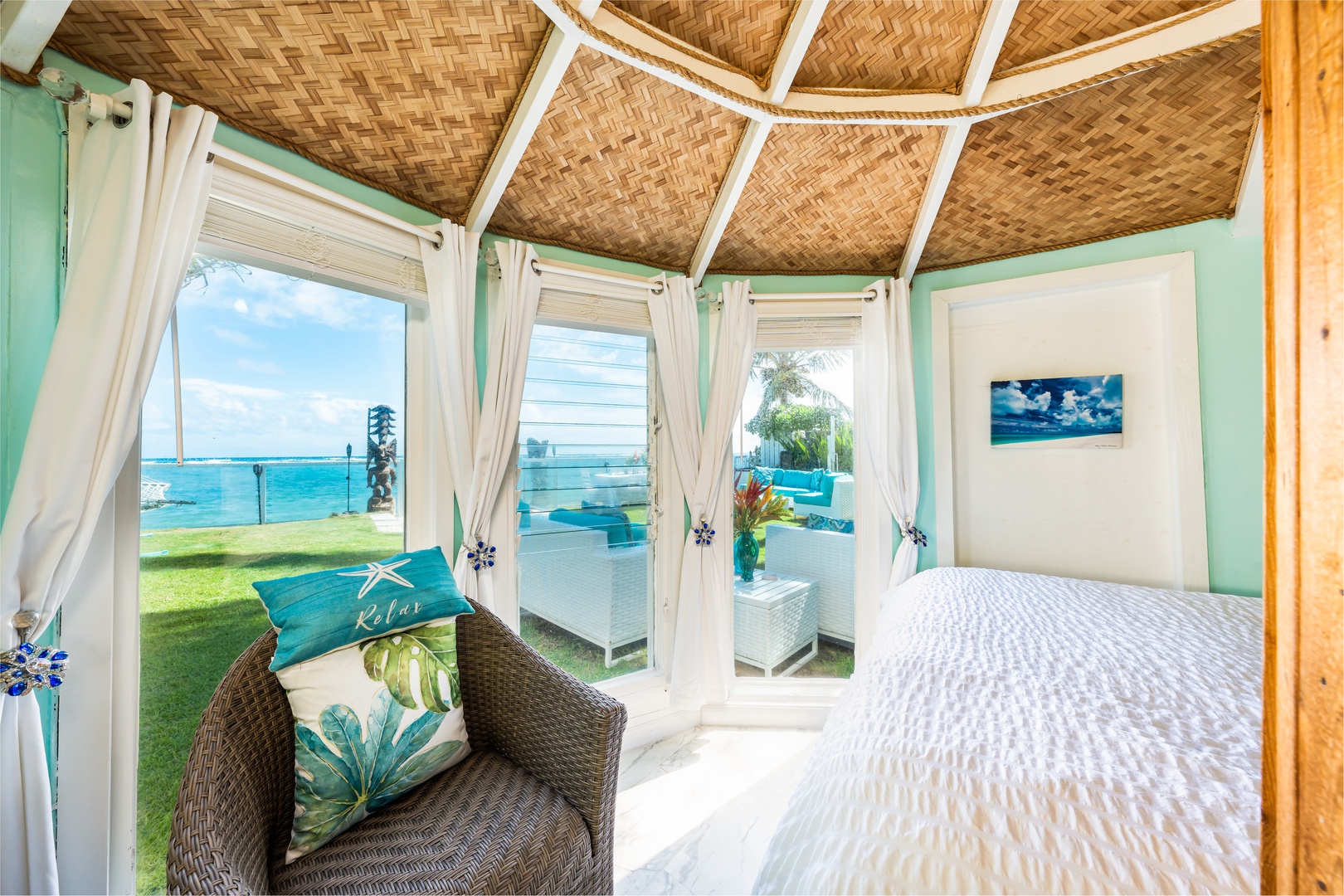 Hauula Vacation Rentals, Private Beach Paradise - A woven bamboo ceiling arches over a bed that faces the ocean through wide windows.