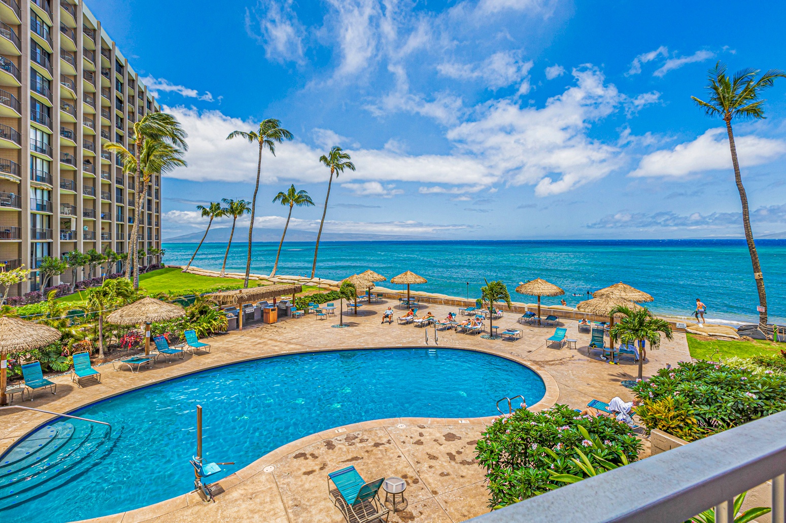 Lahaina Vacation Rentals, Royal Kahana 308 - This image captures a stunning beachfront pool area with clear blue water, surrounded by lounge chairs and tropical umbrellas