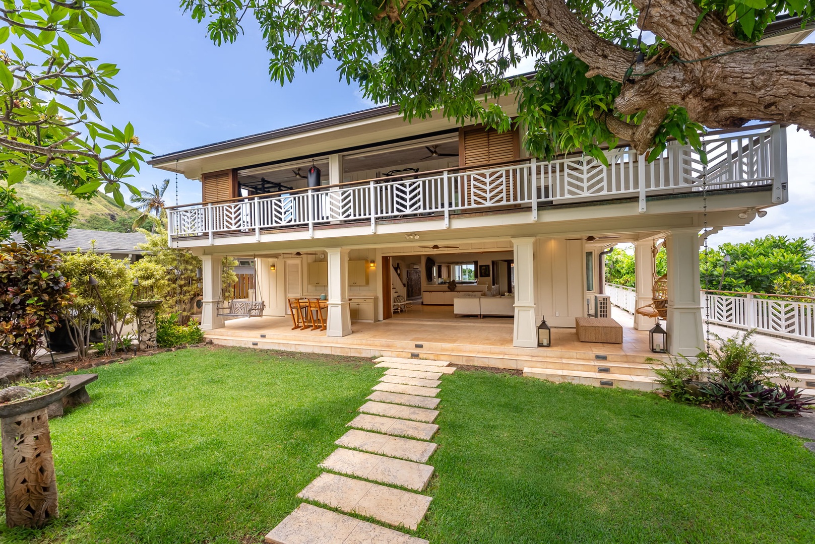 Kailua Vacation Rentals, Leaf House - Two-story island-style vacation home with decorative railings, open-air design, lush green lawn, and tropical landscaping under sunny skies.