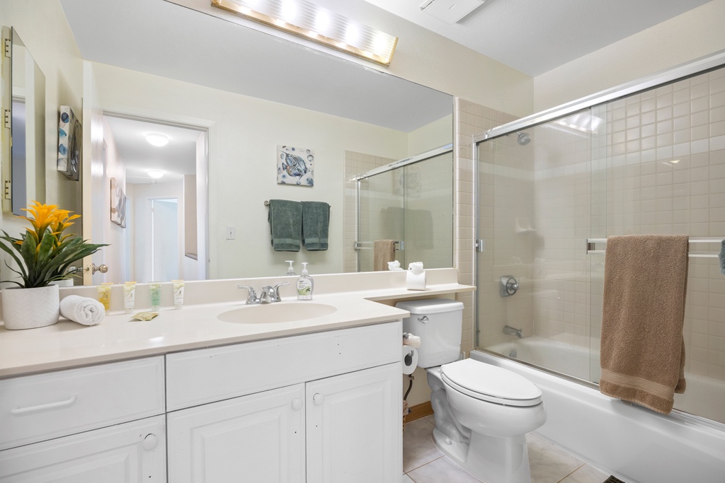 Your bright, beautifully appointed bathroom offers a spacious glass shower, elegant vanity, and thoughtful touches like fresh towels and plants.
