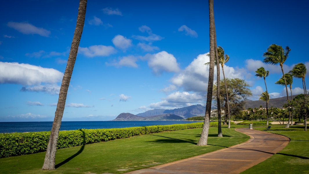 Ko Olina features manicured grounds with palm trees and walking paths, with dramatic mountain views across the bay in the surrounding area.
