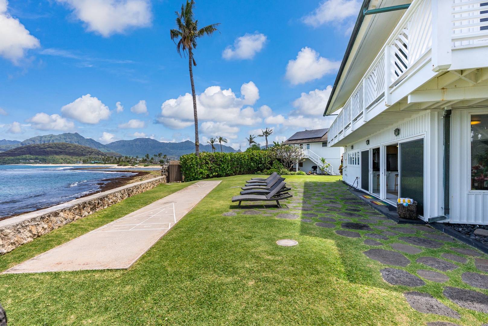 Waianae Vacation Rentals, Ma'ili Blue Estate - A beachfront property featuring pristine lawn area with lounge chairs overlooking tropical coastline and dramatic mountain backdrop.