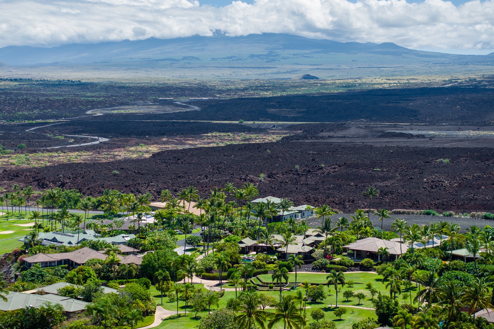 Kamuela Vacation Rentals, Mauna Lani Champion Ridge 22 - An aerial view showcasing tropical homes with a backdrop of lush mountains and volcanic terrain.