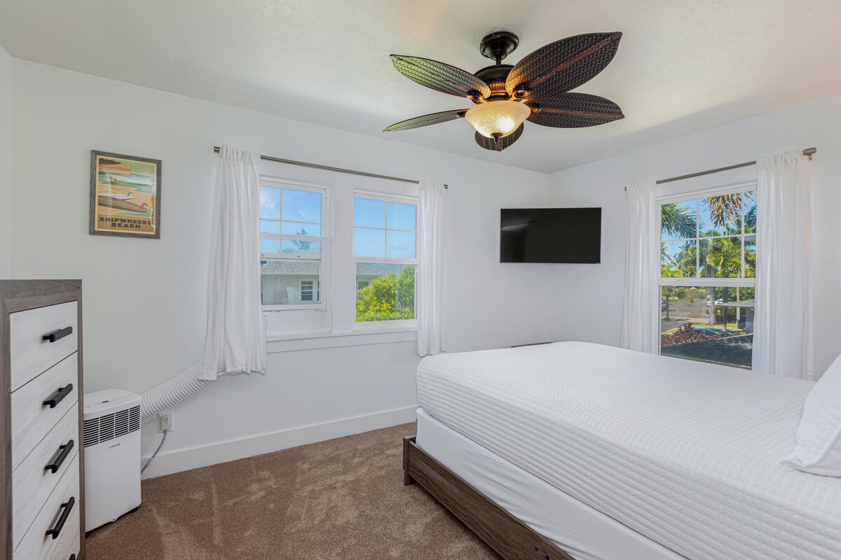 Princeville Vacation Rentals, Pili Aloha - Guest bedroom with ceiling fan, queen bed, and peaceful green views through large windows.