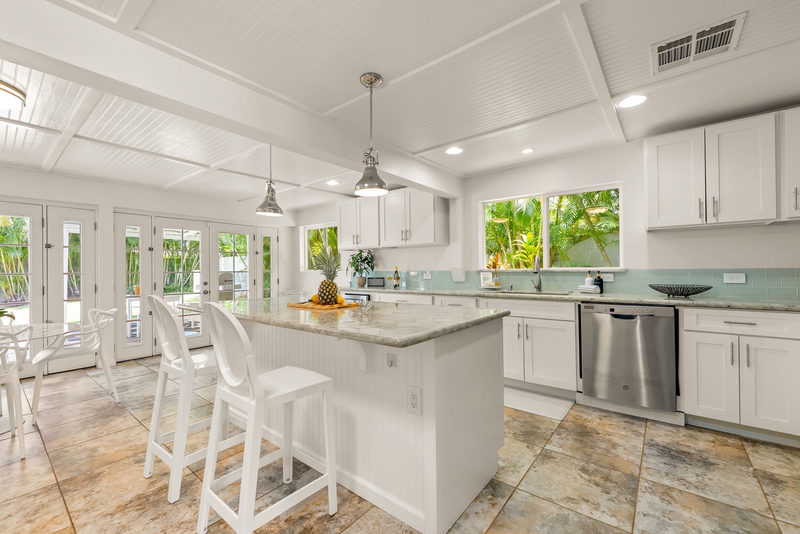 Honolulu Vacation Rentals, Ho'okipa Villa - Step into your bright, coastal-inspired kitchen with white cabinetry, granite counters, and stainless appliances. Large windows frame lush palm views, flooding the space with natural light.