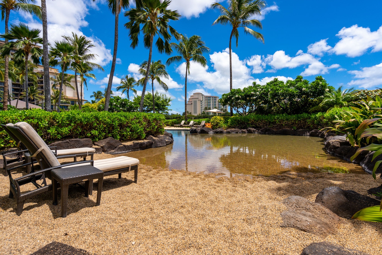 Kapolei Vacation Rentals, Ko Olina Beach Villas B604 - Tropical lagoon setting with palm trees, lounge chairs, and resort buildings creating a peaceful Hawaiian-style retreat.
