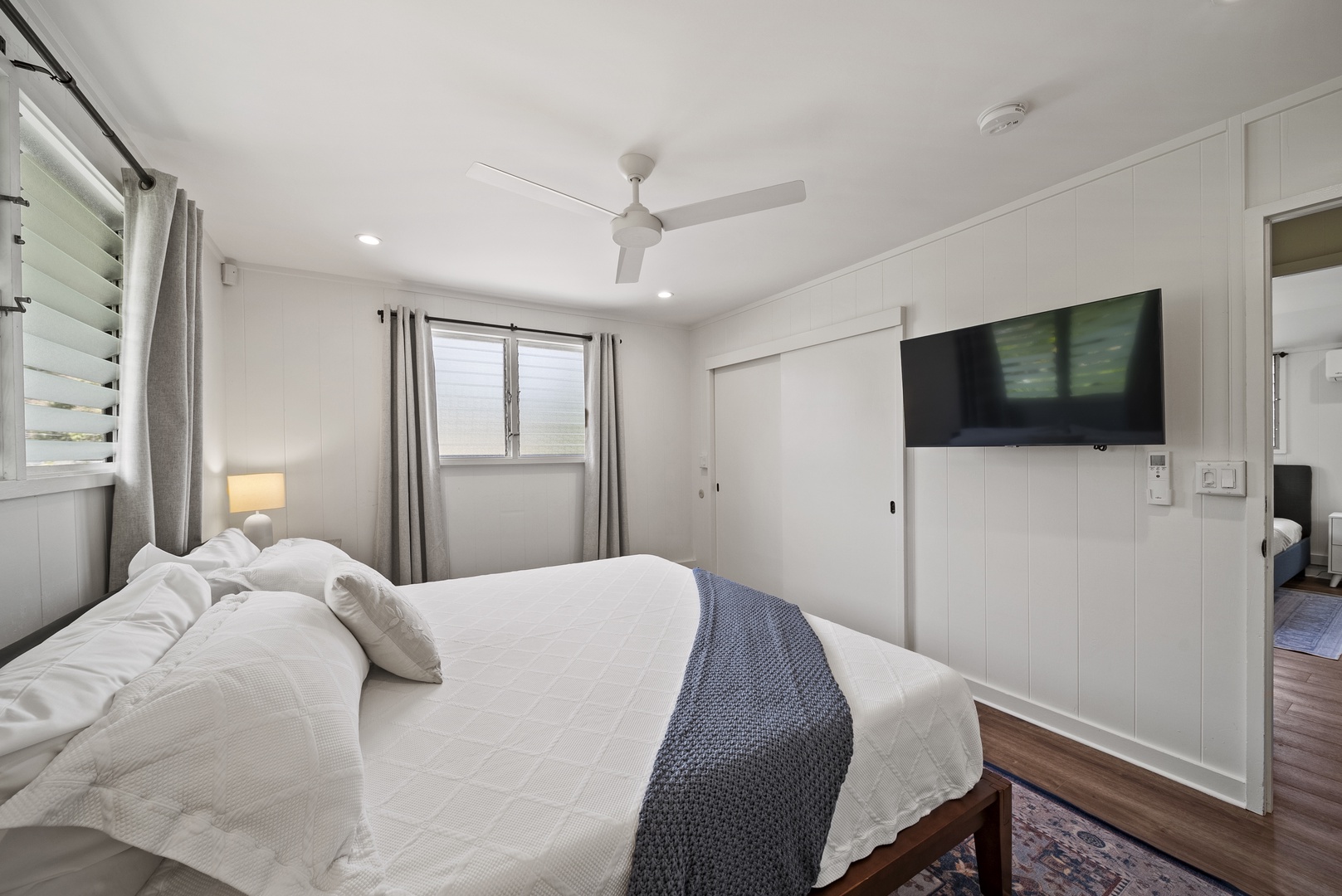 Honolulu Vacation Rentals, Honolulu Beachfront Retreat - Spacious guest suite with a wall-mounted TV, ceiling fan, and plush bedding — perfect for relaxing after exploring Oahu.
