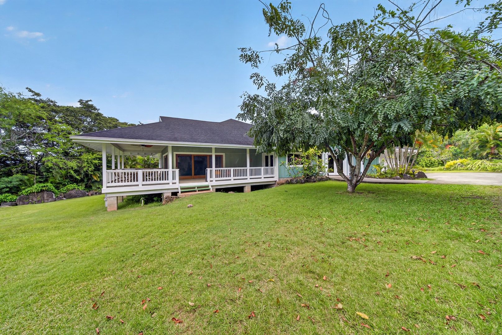 Haleiwa Vacation Rentals, North Shore Tropical Hale - A charming plantation-style home nestled on a lush green lawn, surrounded by tropical foliage and mature trees, with a welcoming covered porch perfect for relaxation.