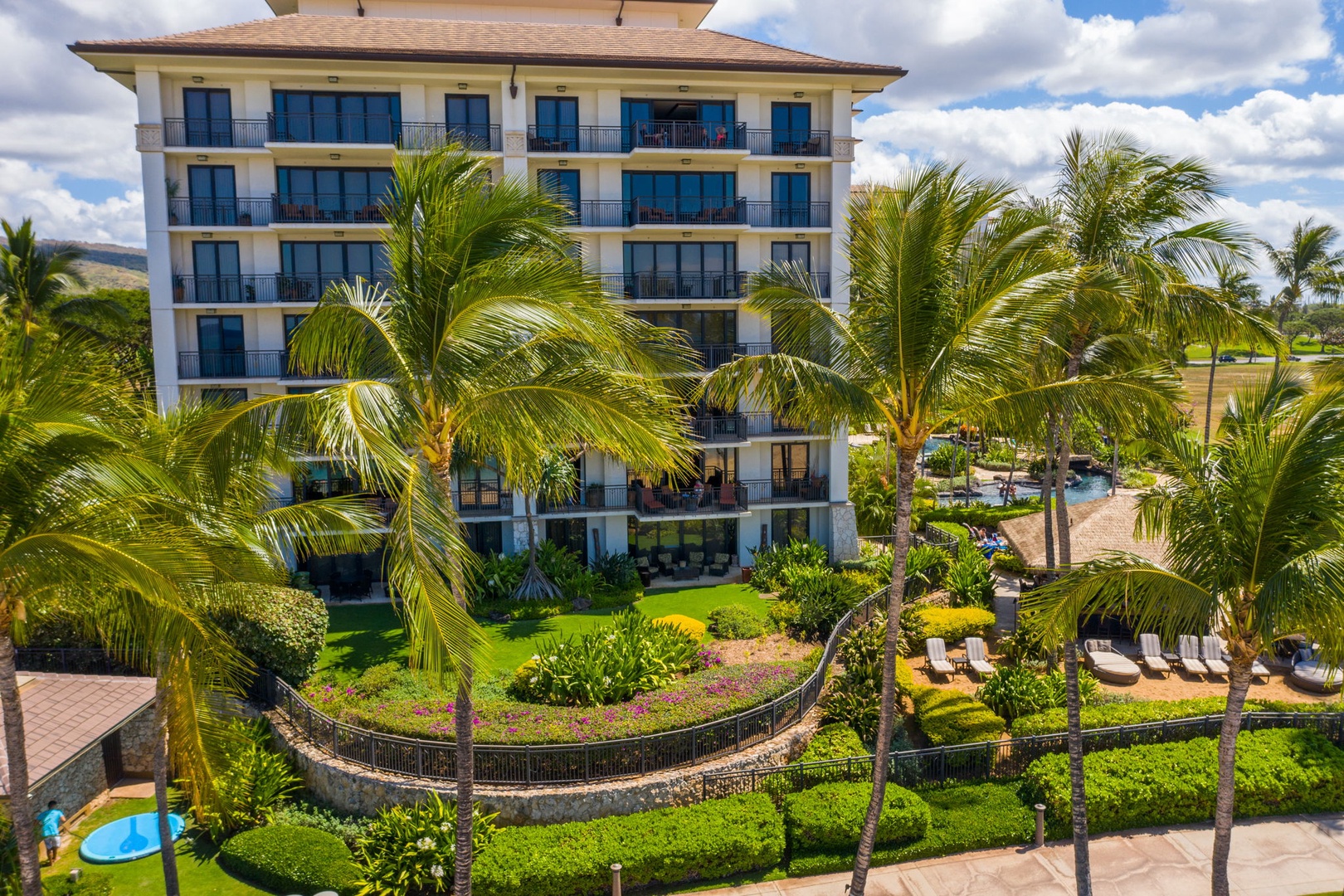 Kapolei Vacation Rentals, Ko Olina Beach Villas B604 - Multi-story resort building surrounded by lush tropical gardens and swaying palm trees under bright blue skies.