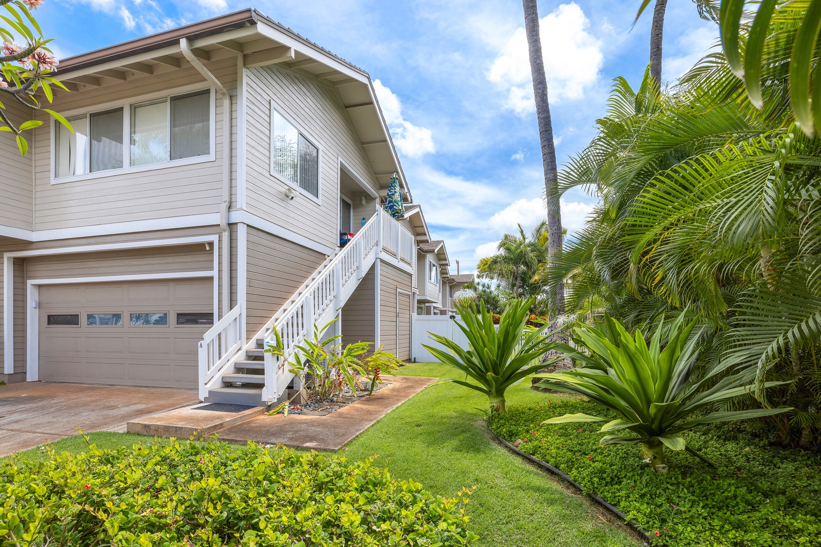 Two-story beige property with white trim nestled among tropical palms and lush landscaping.