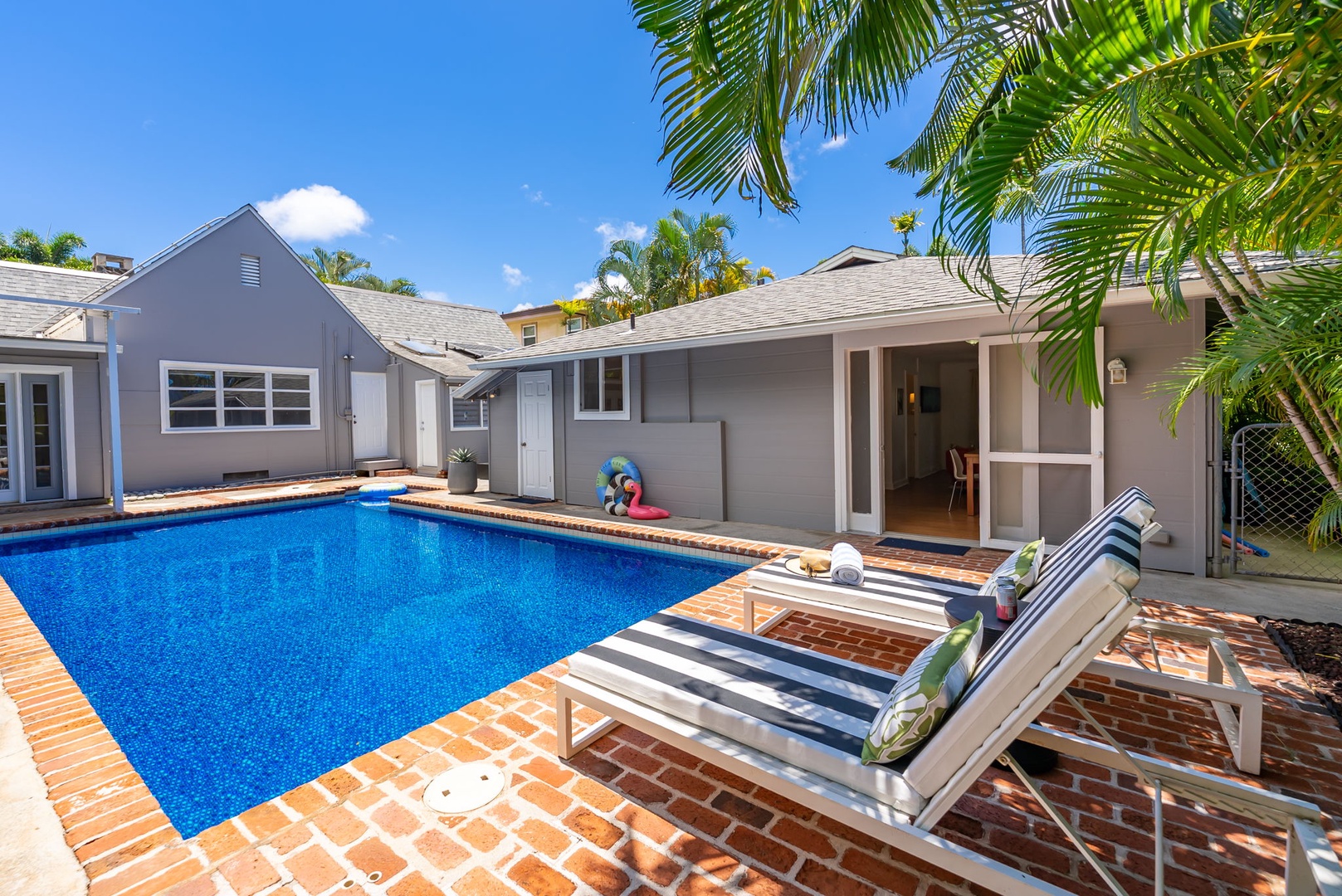 Honolulu Vacation Rentals, Ho'okipa Villa - A secluded outdoor retreat featuring a sparkling private pool, sun-soaked brick deck, and shaded loungers framed by tropical palms—your perfect spot to unwind under blue skies.