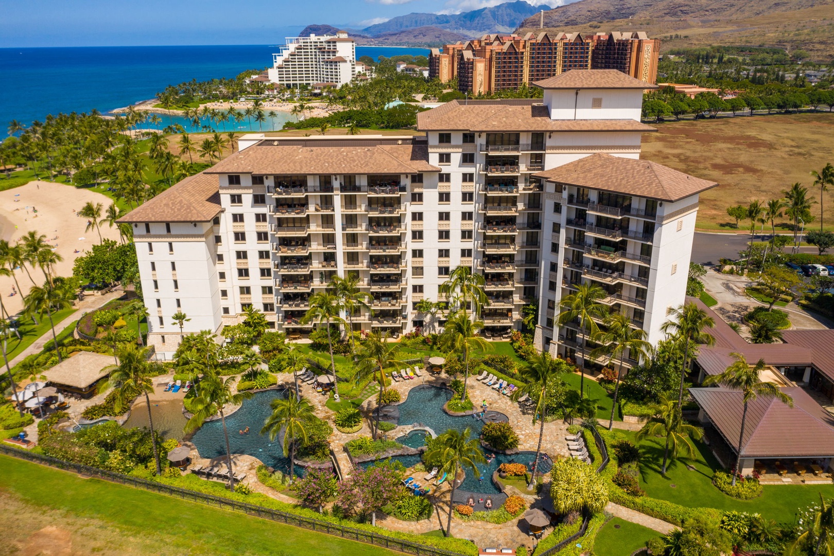 Kapolei Vacation Rentals, Ko Olina Beach Villas B604 - Resort complex featuring luxury towers, lagoon-style pool, and tropical landscaping near pristine beach and mountain backdrop.