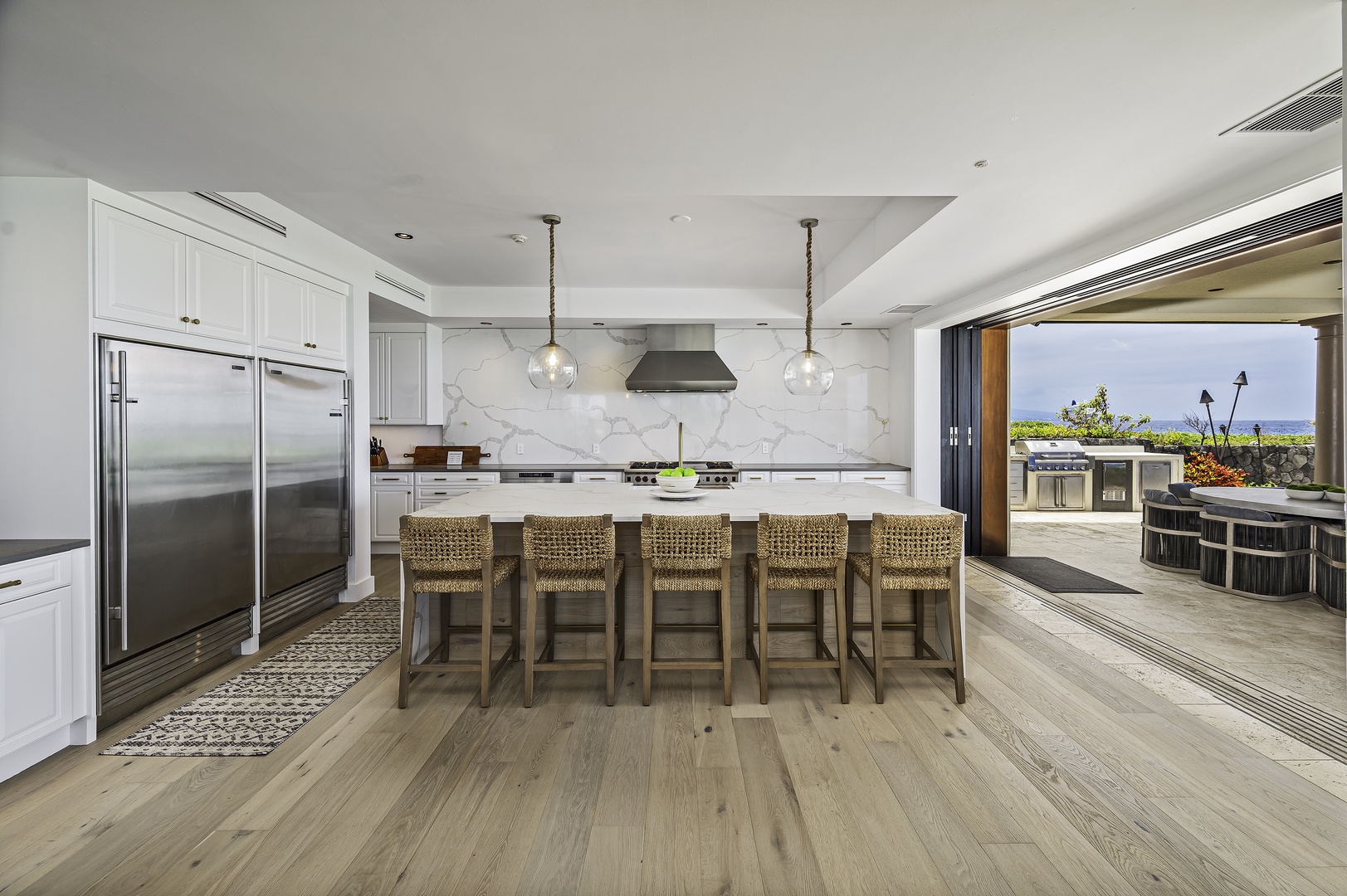 Kailua Kona Vacation Rentals, Alohi Kai Estate • - Wide open kitchen with all high end quartz material and top of the line appliances from Wolf and Sub zero with huge entertaining island and perfectly complimented by Nautical designed rattan bar chairs and rope wrapped pendant lights