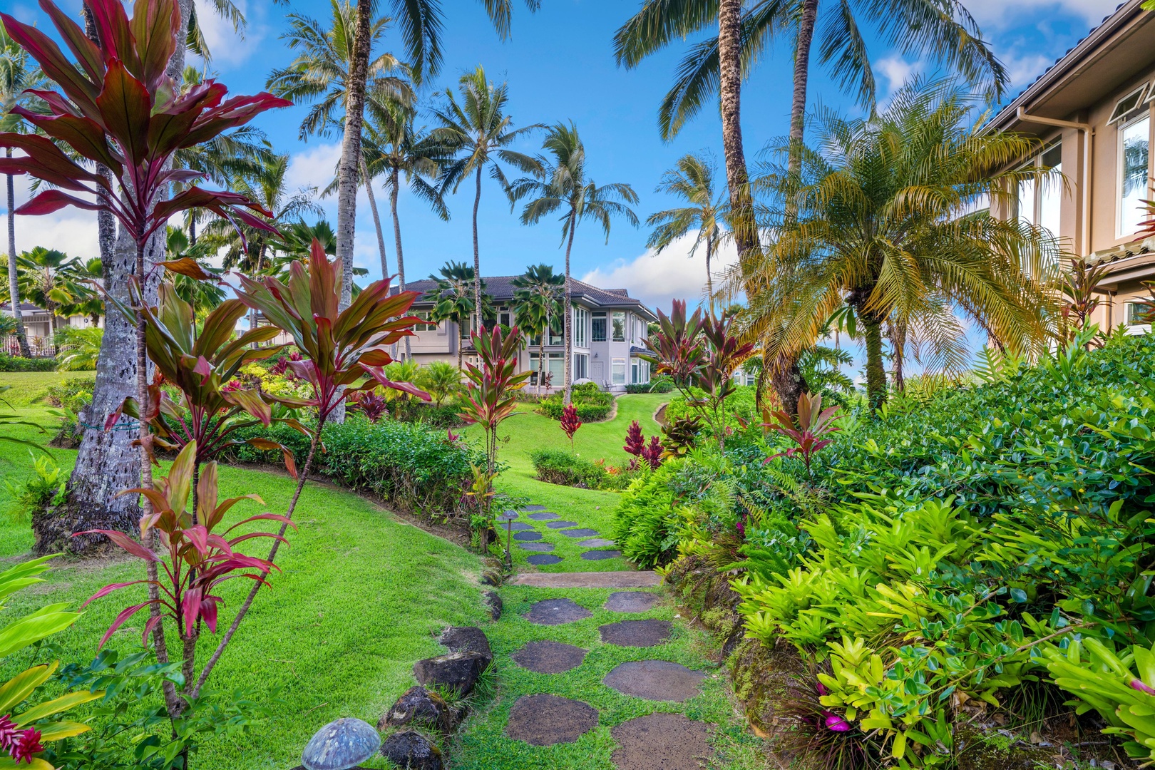 Princeville Vacation Rentals, Noelani Kai - A stepping-stone path winds through palms and red ti leaves, a mid-day walk ready to be taken.