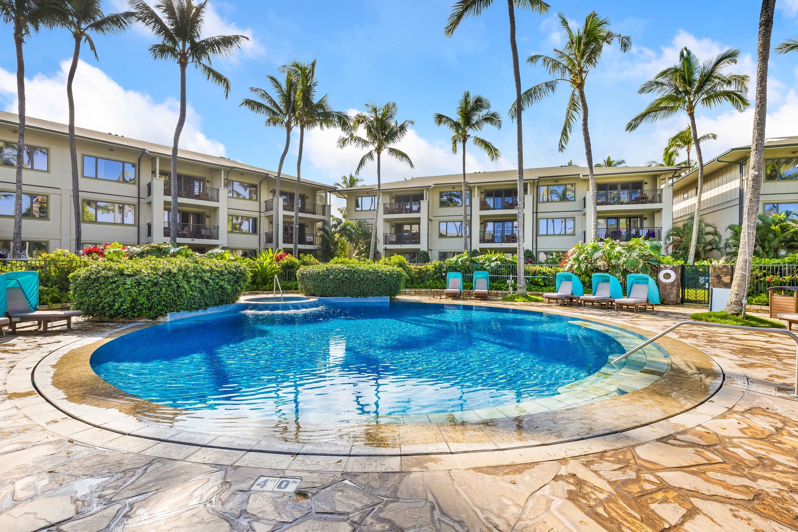 Kahuku Vacation Rentals, Turtle Bay Villas 209 - Tropical resort complex featuring a sparkling pool surrounded by swaying palm trees and modern multi-story buildings.
