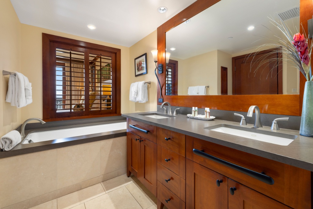 Kapolei Vacation Rentals, Ko Olina Beach Villas B410 - Elegant ensuite bathroom with a large mirror, dual sinks, and a bathtub, featuring wooden accents and natural lighting.