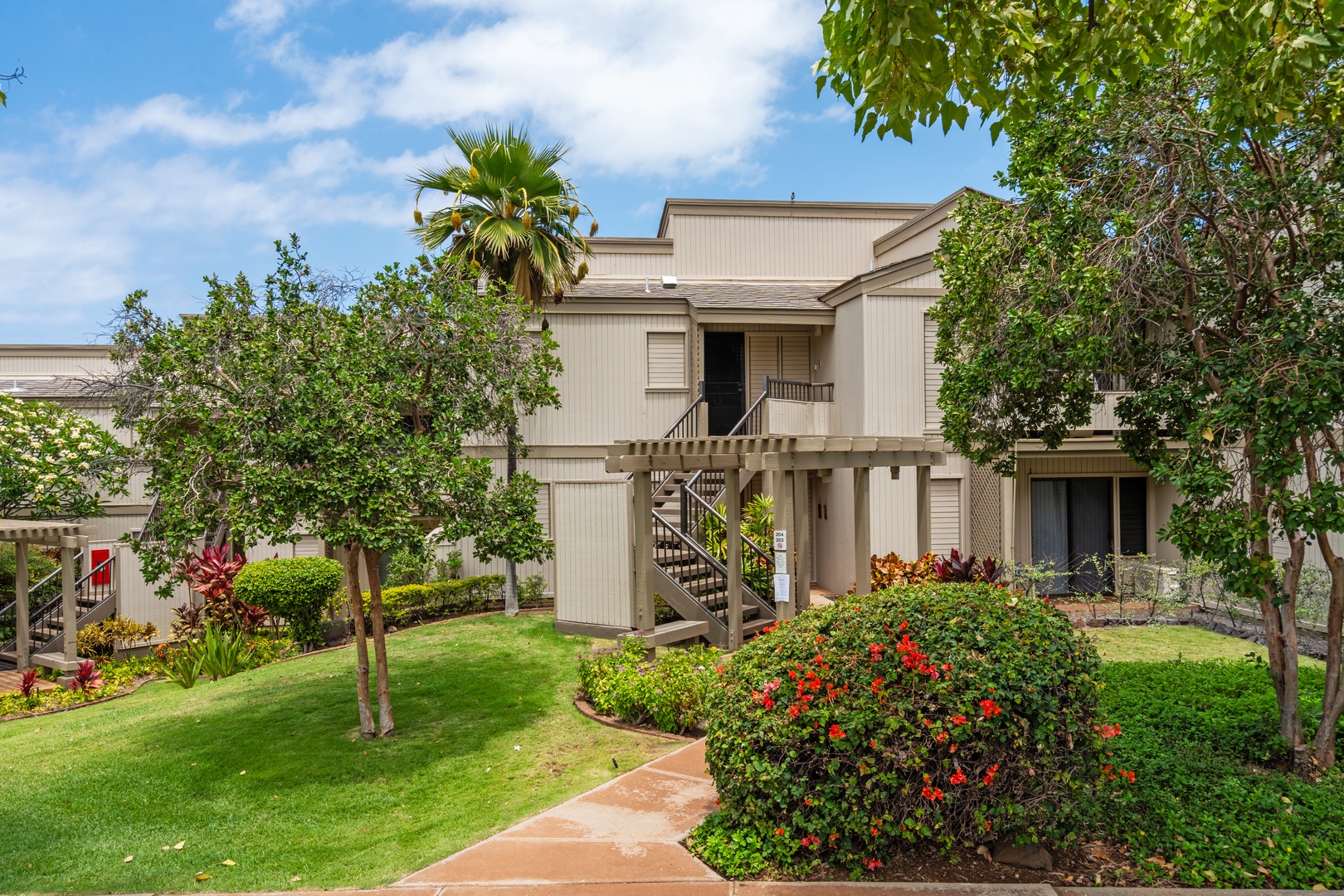 Kihei Vacation Rentals, Wailea Ekolu 204 - A stone path winds through red hibiscus and green lawn to the stairway leading up to the front door.