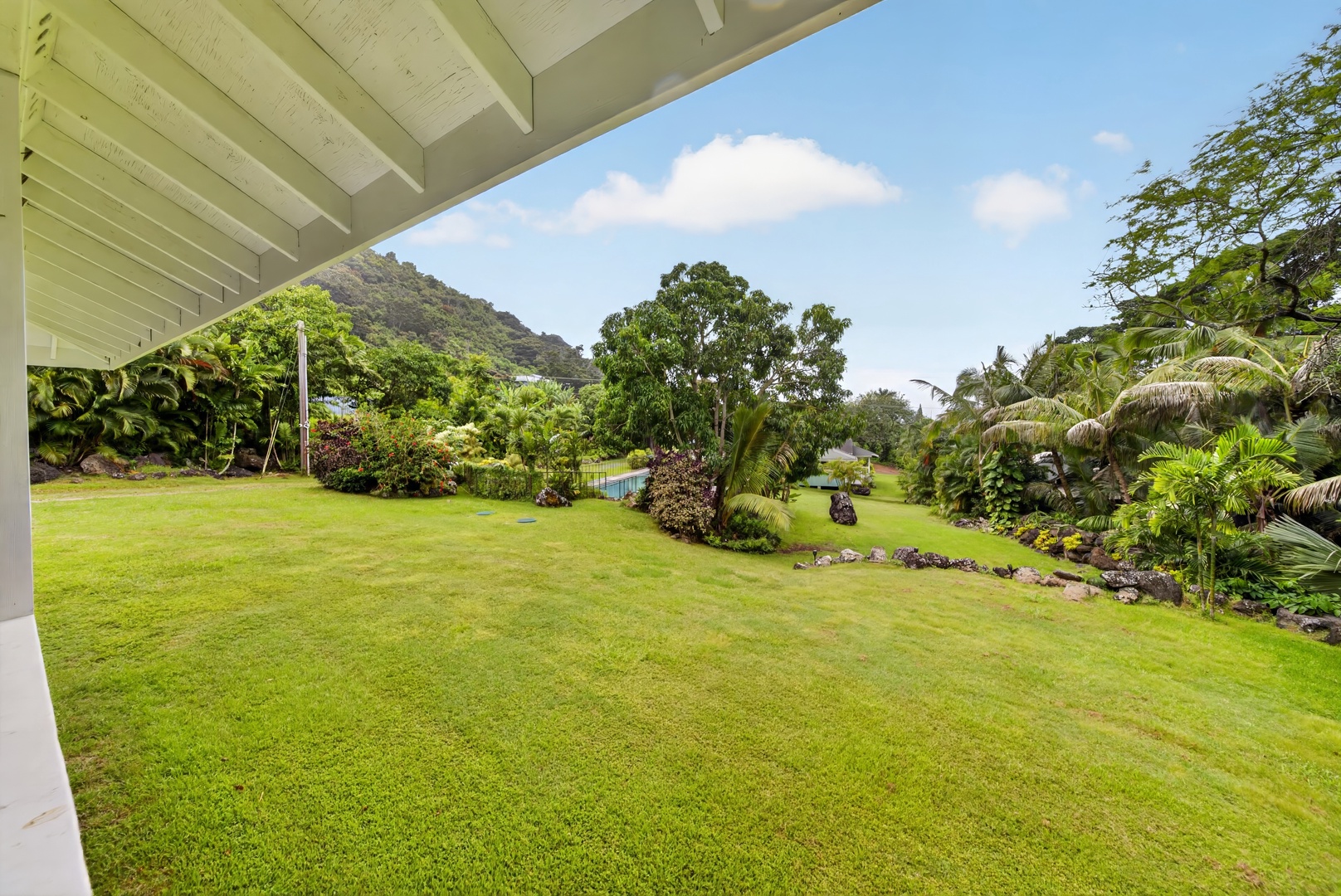 Haleiwa Vacation Rentals, North Shore Tropical Hale - Expansive tropical garden framed by covered lanai, featuring lush lawn and mountain backdrop—part of the property's surrounding outdoor environment.