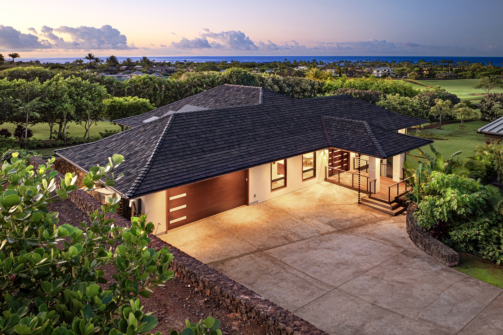 Koloa Vacation Rentals, Hale Kai‘opua at Kukui'ula - Aerial view of the home's entrance surrounded by lush greenery and a serene ocean backdrop.