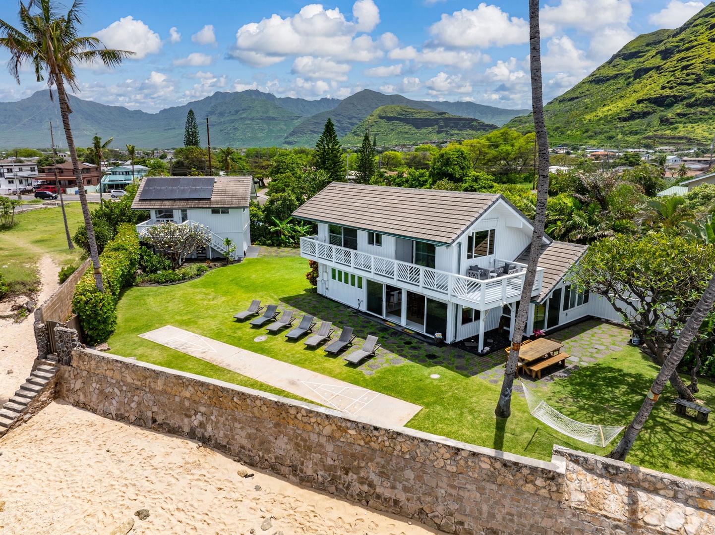 Waianae Vacation Rentals, Ma'ili Blue - Aerial view showcasing a pristine oceanfront property nestled between lush tropical mountains and residential neighborhoods in a stunning Hawaiian setting.