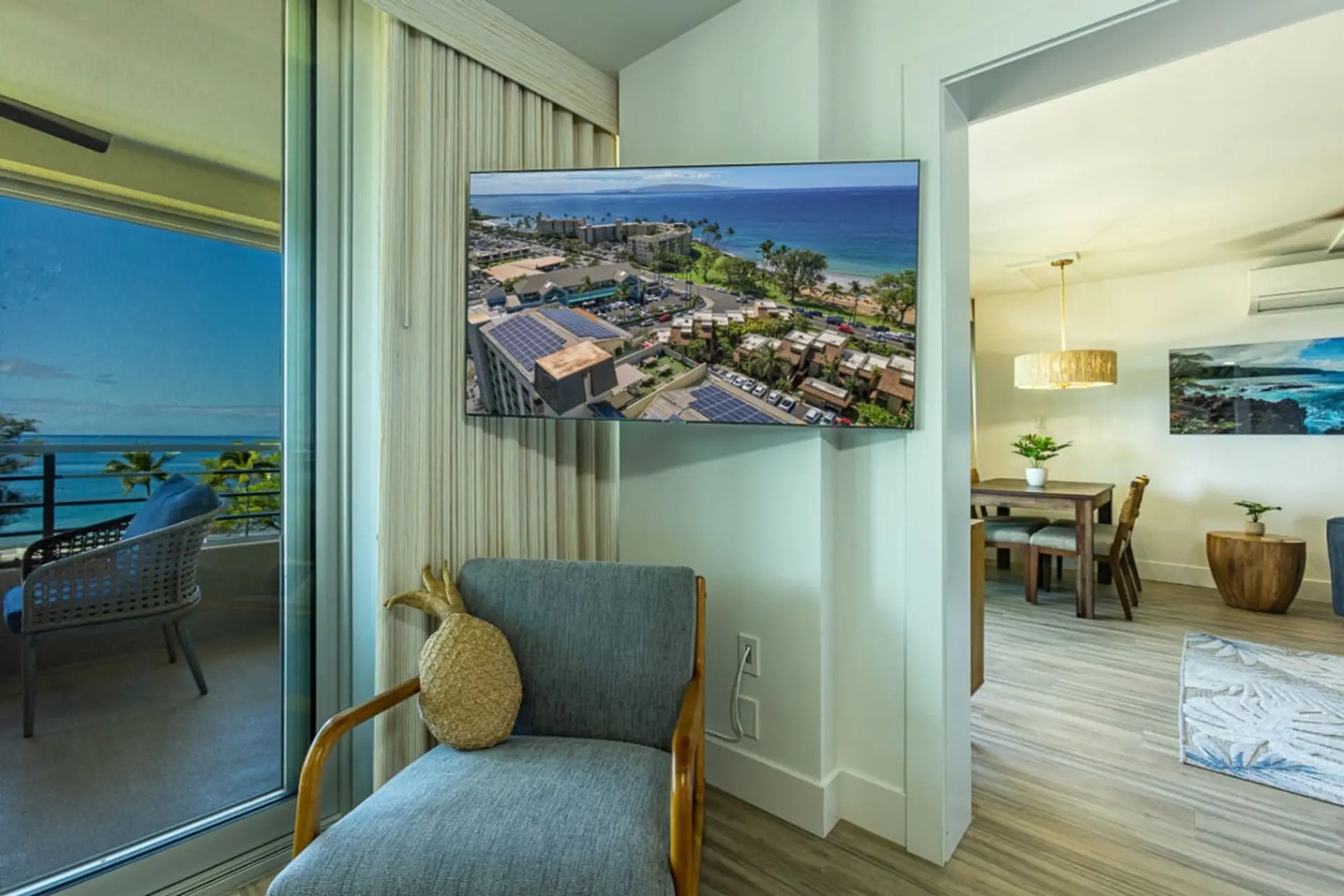 Kihei Vacation Rentals, Kamaole Beach Royal 610 - A wall-mounted TV and a pineapple-pillowed chair mark the corner between the living and dining rooms.