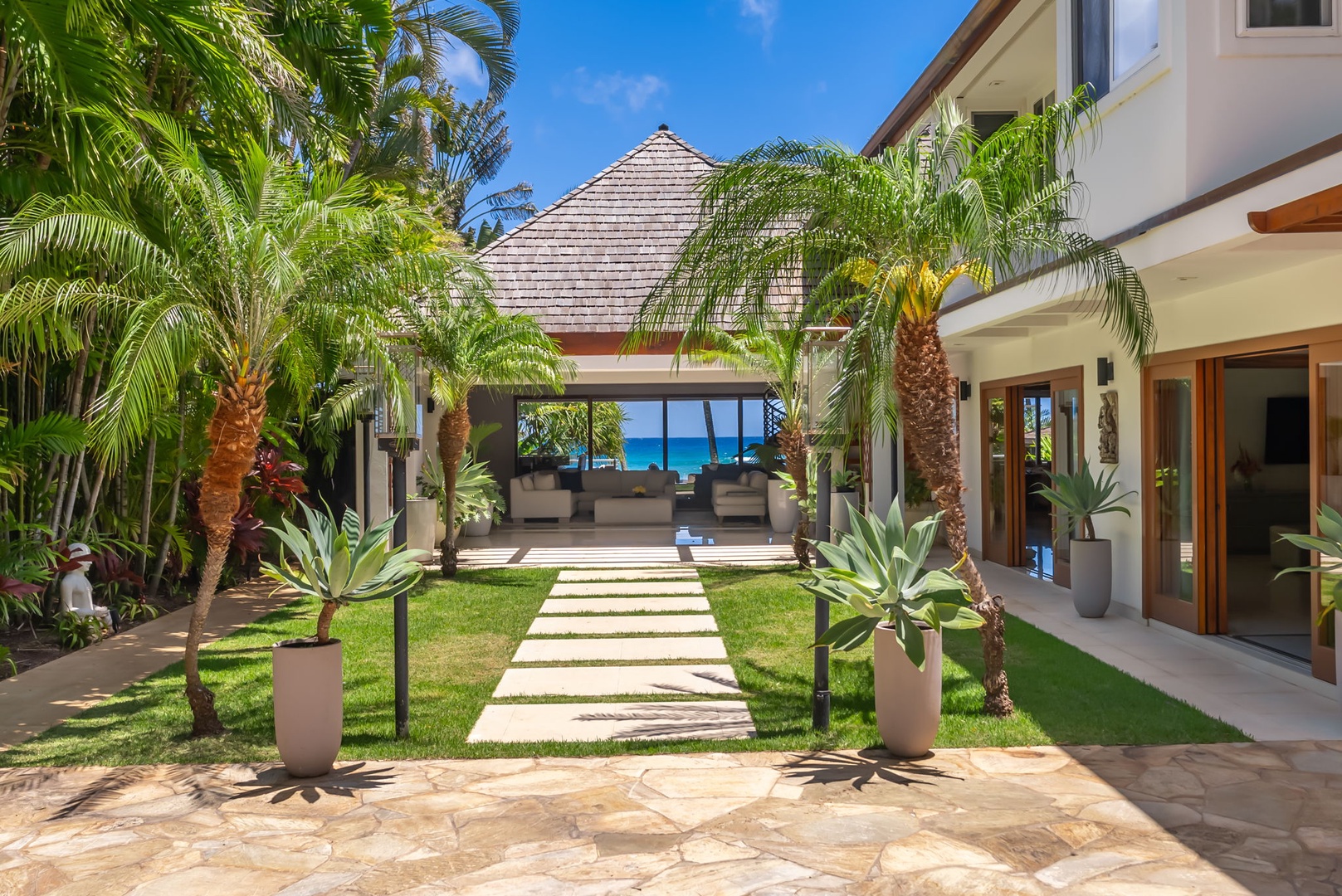 Honolulu Vacation Rentals, Diamond Head Beachfront Estate - Tropical paradise meets modern luxury: a pristine stone pathway guides you through lush palms toward serene ocean views, where indoor-outdoor living creates your perfect beachfront escape.