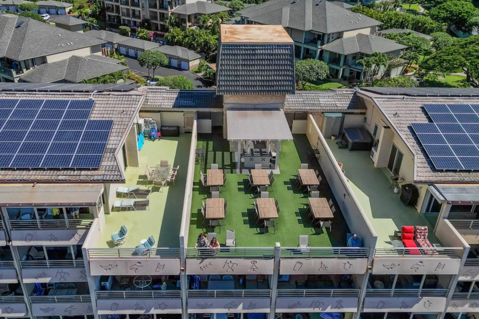 Kihei Vacation Rentals, Kamaole Beach Royal 610 - A turf-covered rooftop terrace holds rows of dining tables under a wood pergola, seven floors up.